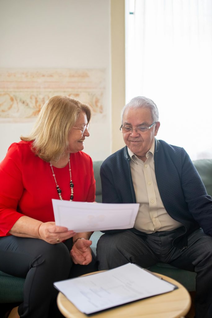 pexels-photo-8439686-8439686 Senior couple consulting on pension options, smiling on a sofa, discussing documents.